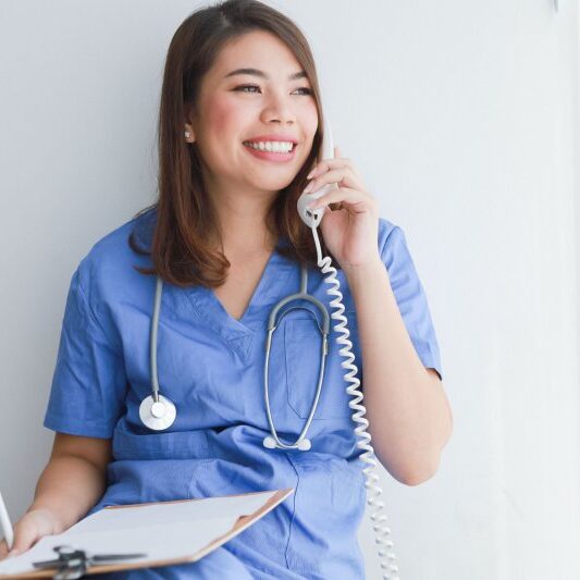 Asian woman in blue doctor uniform using telephone on white background