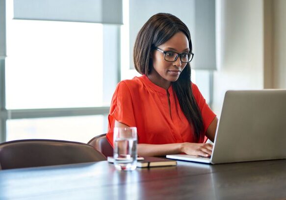 Attractive young businesswoman sitting alone at a desk in a modern office looking focused while working on a laptop