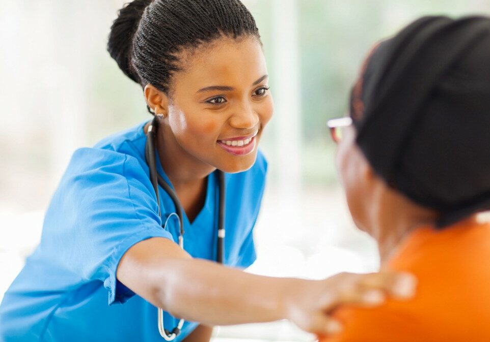 caring african medical nurse comforting senior patient in office